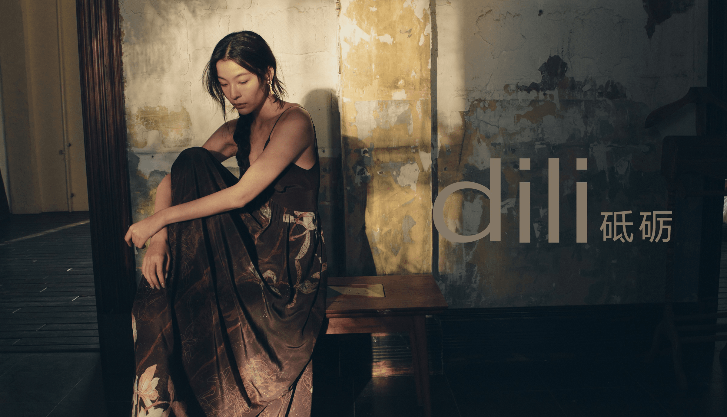 dili editorial hero — model in dark brown slip dress against a weathered wall